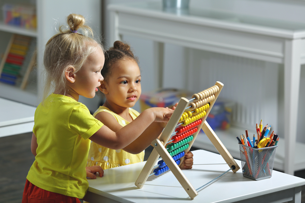 children of different races sit together at the table and count on the abacus
